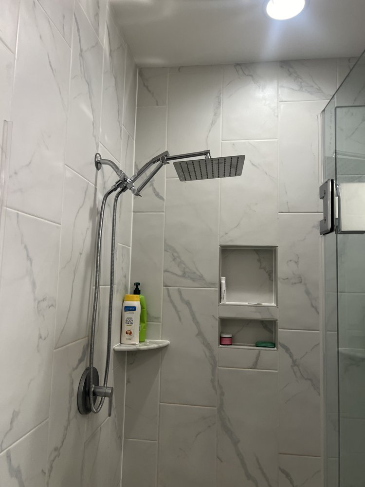 Tiled shower with a handheld shower head on a slide bar and a recessed shelf
