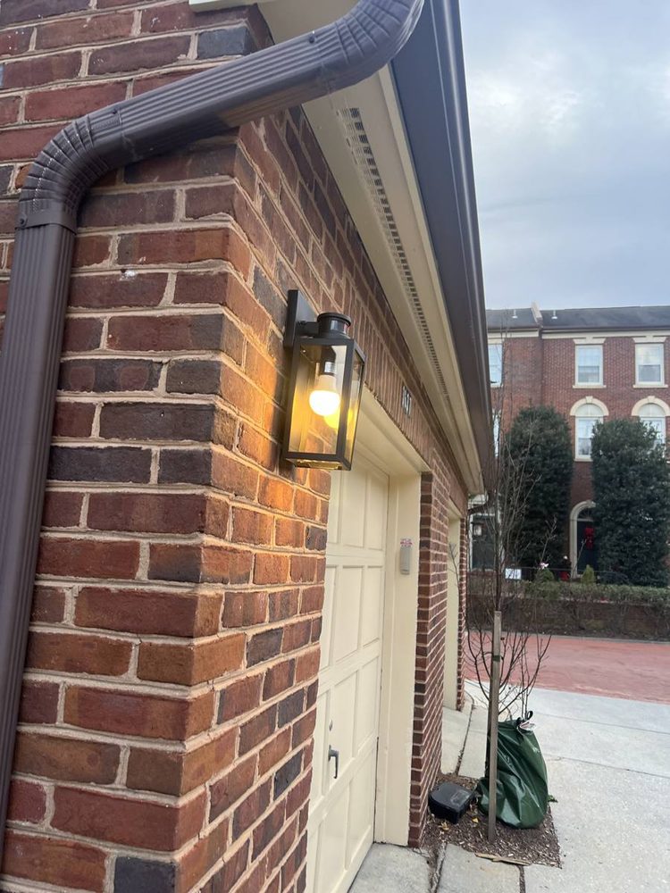 Lit black wall lantern mounted on brick beside a garage