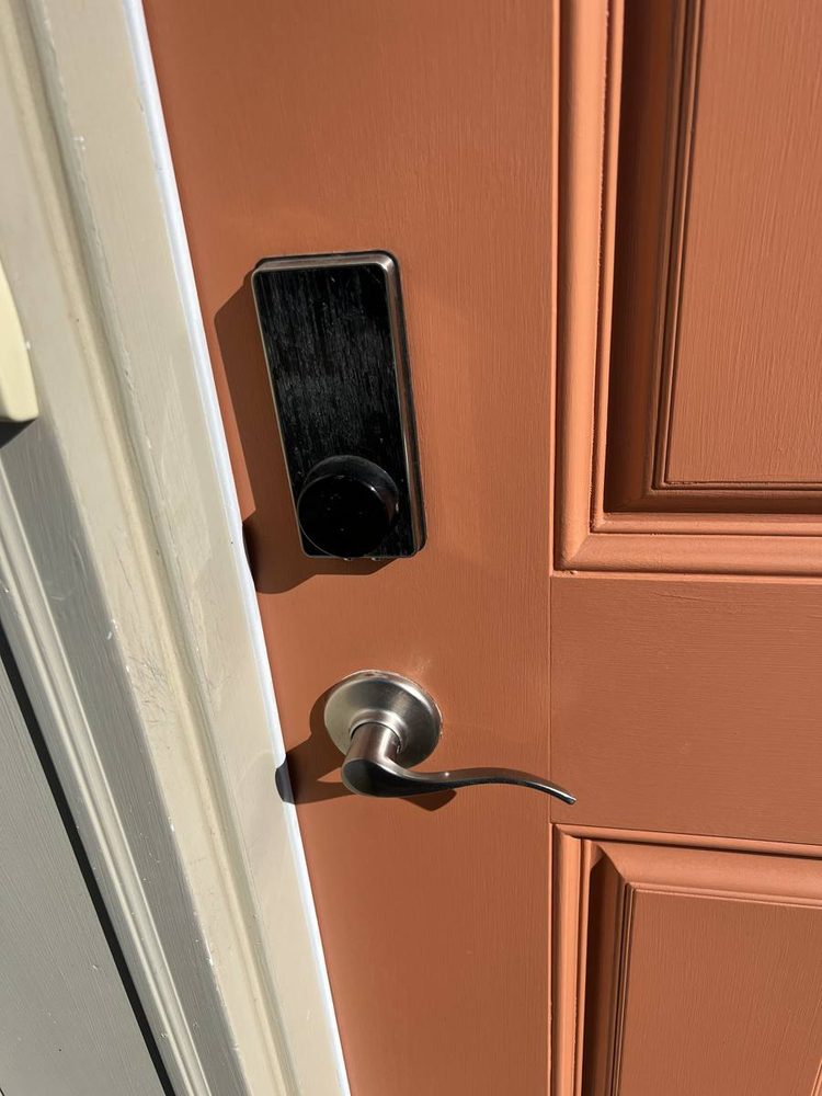Black electronic smart lock installed above a lever handle on a terracotta front door