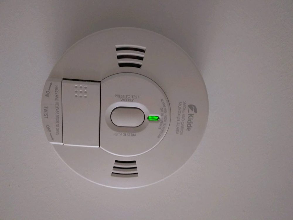 Smoke and carbon monoxide alarm mounted on a ceiling with its green light on