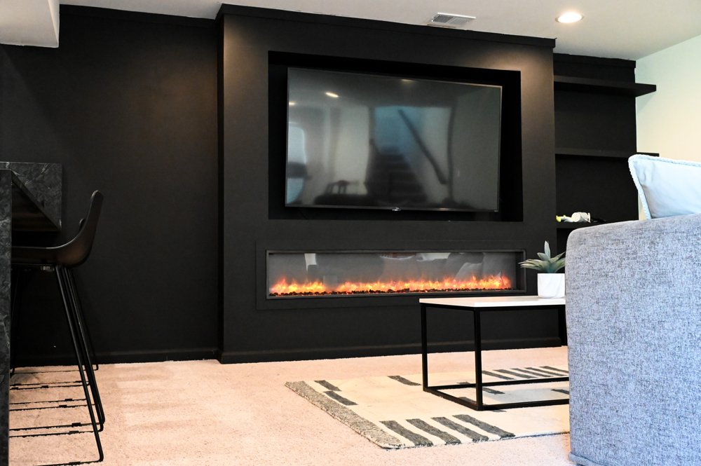 Flat-screen television mounted on a dark feature wall above a linear fireplace with no visible cables