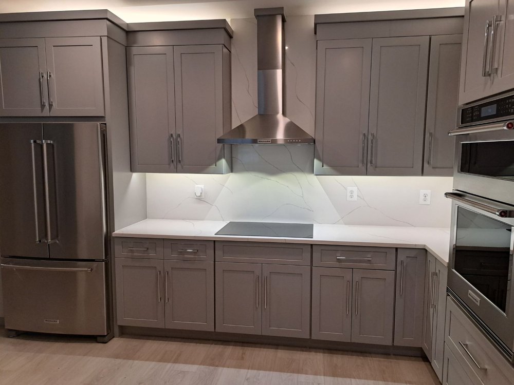Kitchen with gray cabinets and under-cabinet lights illuminating the white backsplash and counter